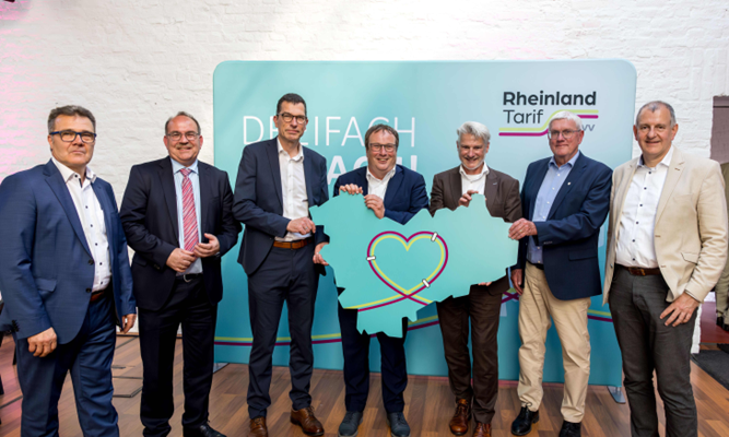 Volker Otto, Dr. Ralf Nolten, AVV-Geschäftsführer Hans-Peter Geulen, Minister Oliver Krischer, VRS-Geschäftsführer Michael Vogel, Sebastian Schuster und Joachim Adler mit einer Karte, die die Umrisse des neuen gemeinschaftlichen Tarifgebiets zeigt.